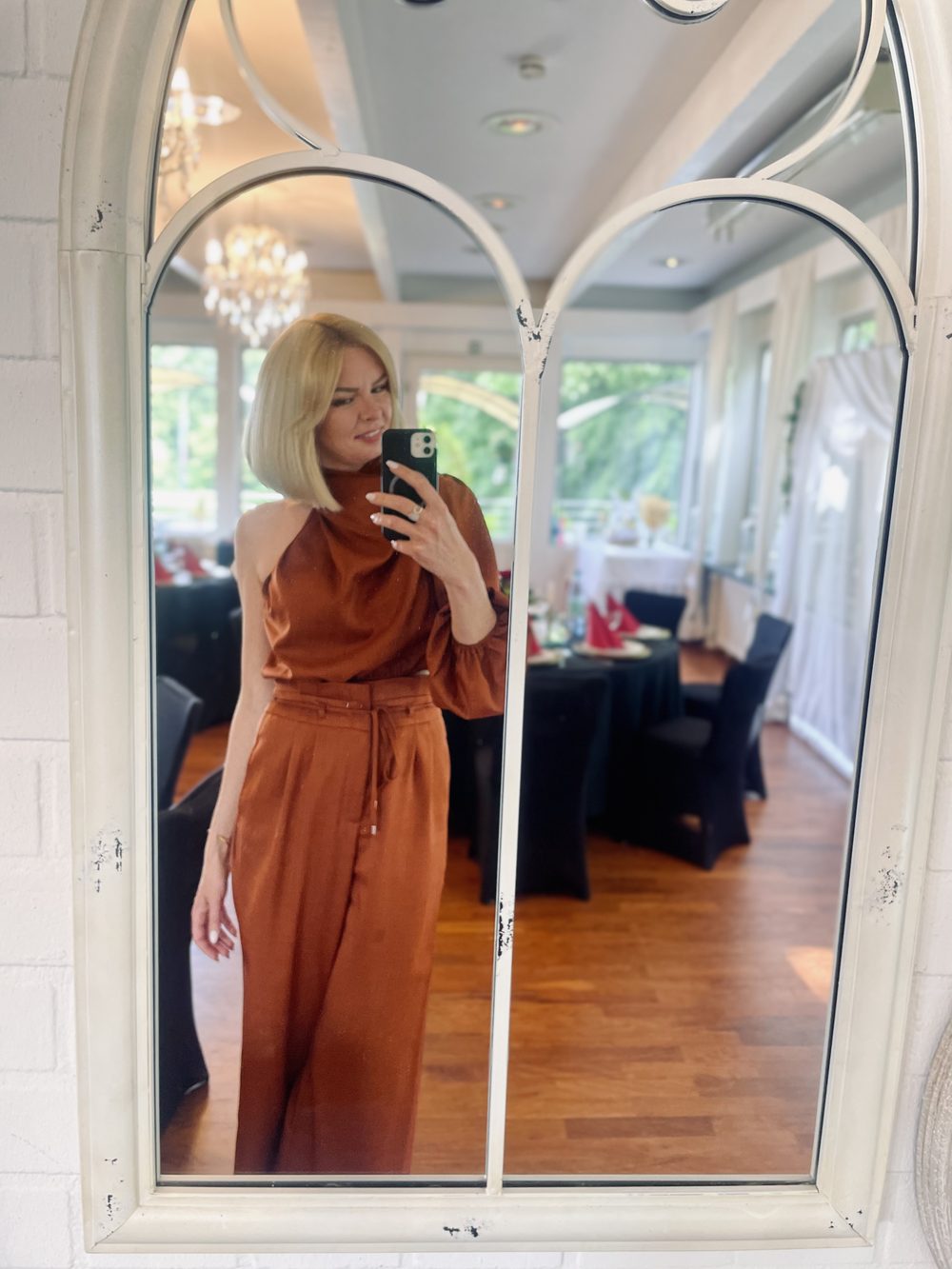 Daria Pfeiffer fotografiert sich im Spiegel eines festlich eingedeckten Saals, in einem eleganten rostbraunen Outfit