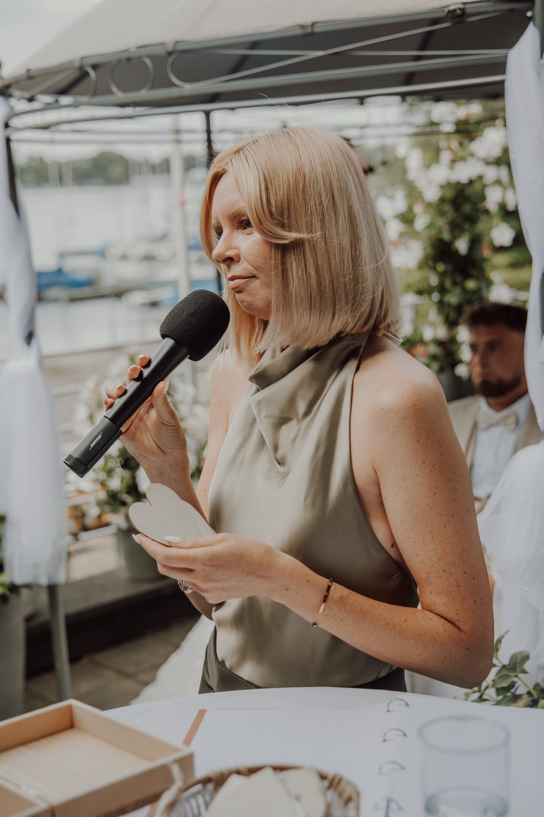 Daria Pfeiffer hält bei einer freien Trauung inne, mit Mikrofon und einem Holzherz in den Händen