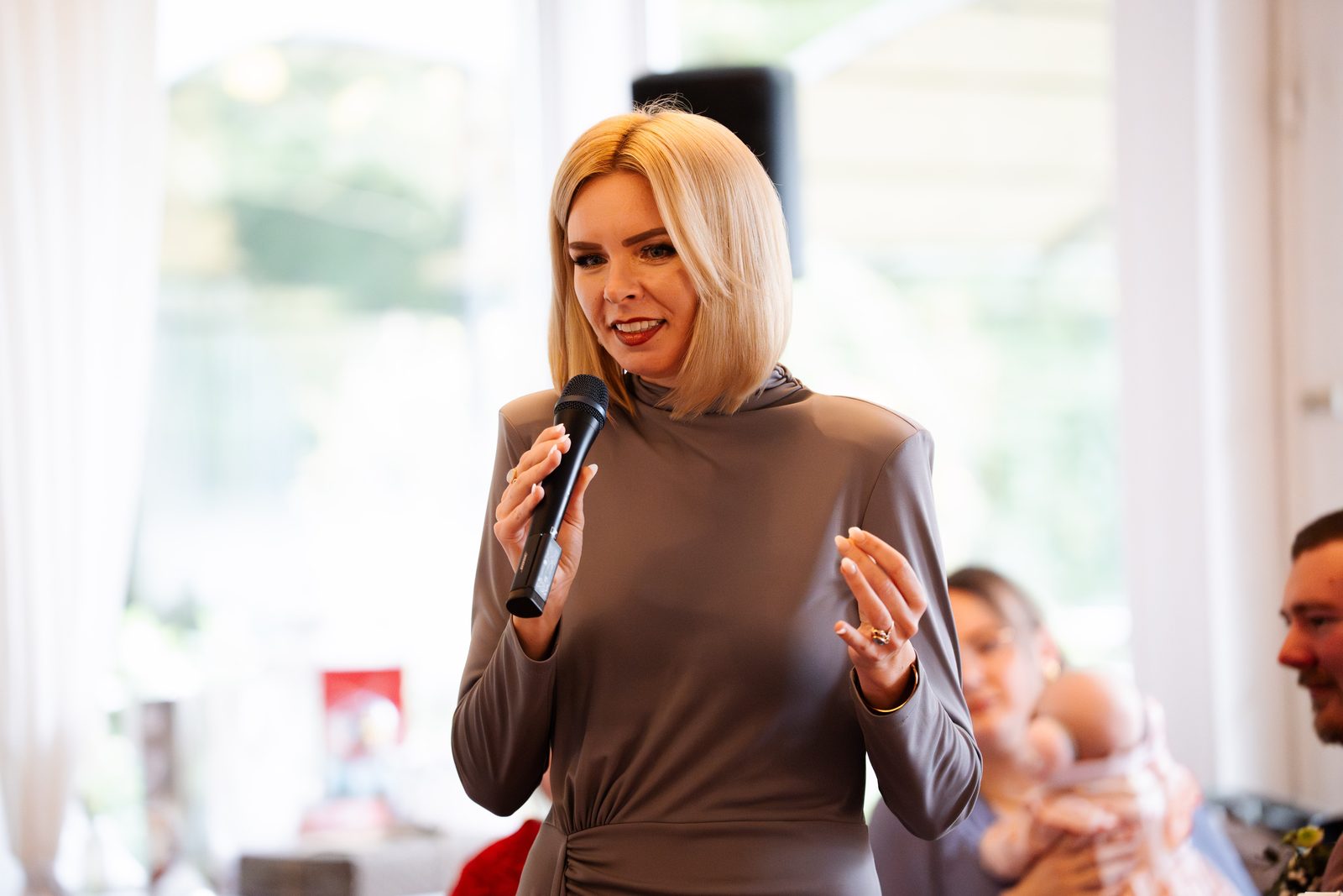 Daria Pfeiffer spricht bei einem Kinderwillkommensfest, im Hintergrund ein Baby auf dem Arm